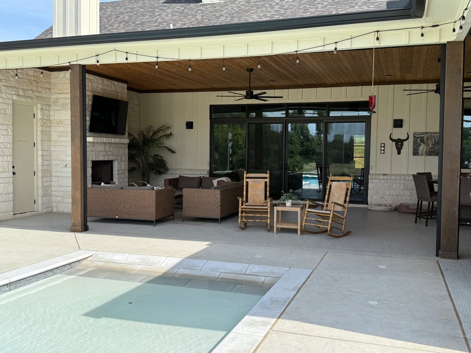 A spacious covered patio with retractable screens, comfortable seating, a fireplace, and a pool — the outdoor room as a natural extension of home.