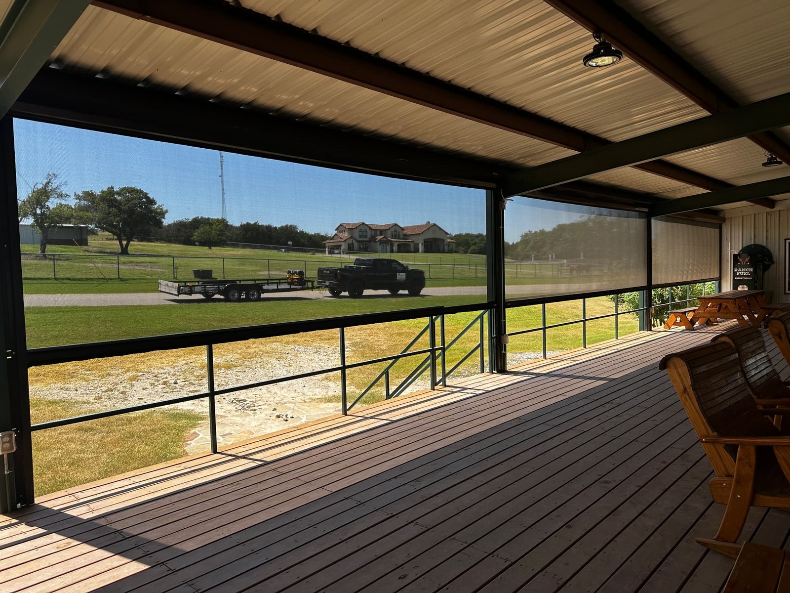 A covered ranch deck with retractable screens overlooking pasture, truck, and distant home.