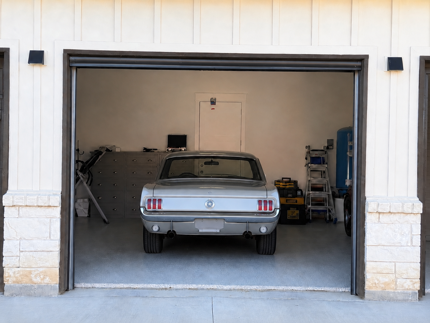A classic first-generation Mustang sits inside a garage, viewed from the exterior through a fully lowered retractable screen.
