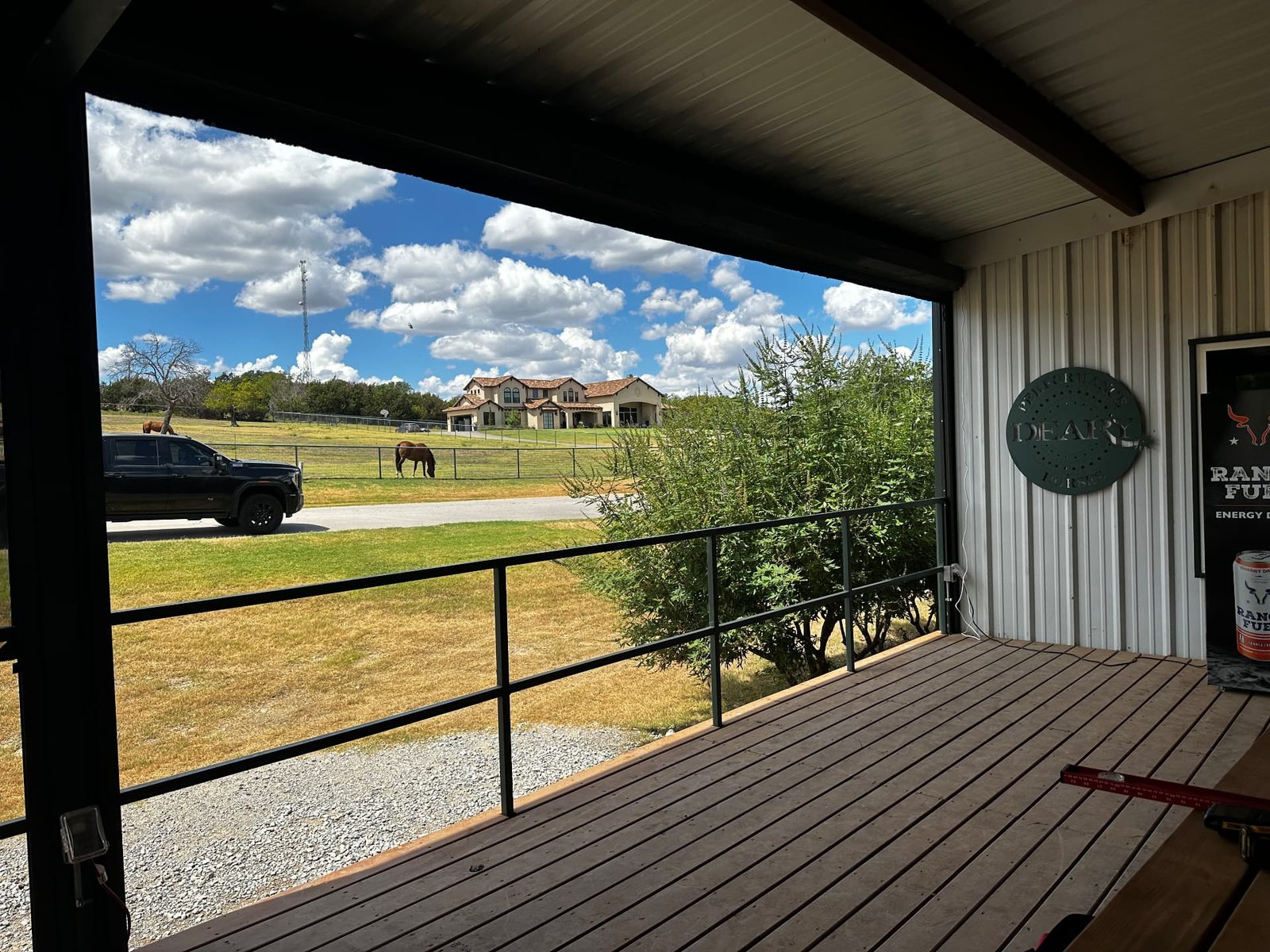 A real ranch deck looking out over pasture, truck, horse, and distant home under a wide Texas sky.