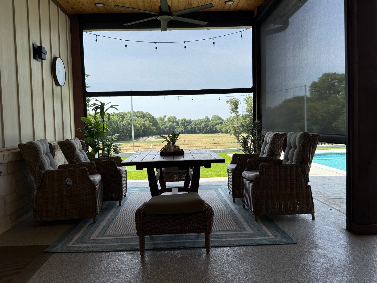 A covered patio dining area with comfortable wicker seating, a wooden table, and a view of the pool and open landscape beyond.