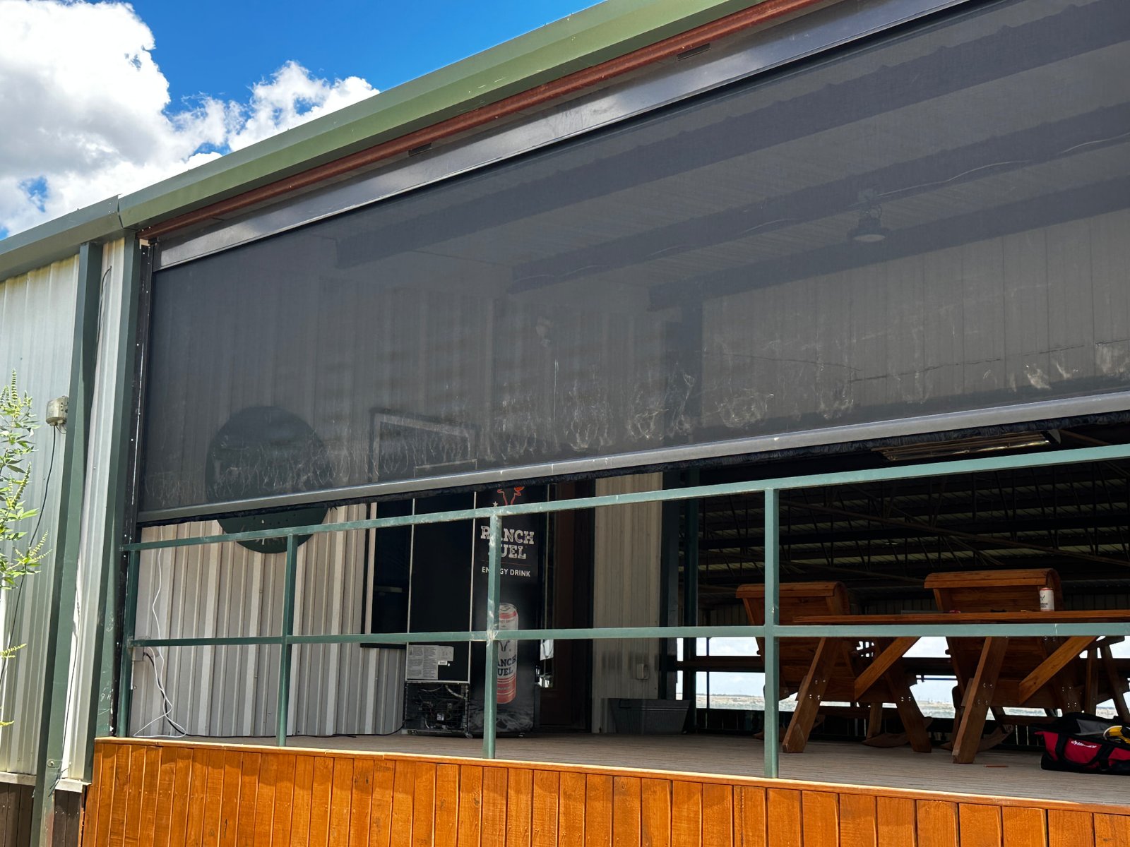 Real exterior photo of a ranch pavilion with a large retractable screen partially lowered over the opening.