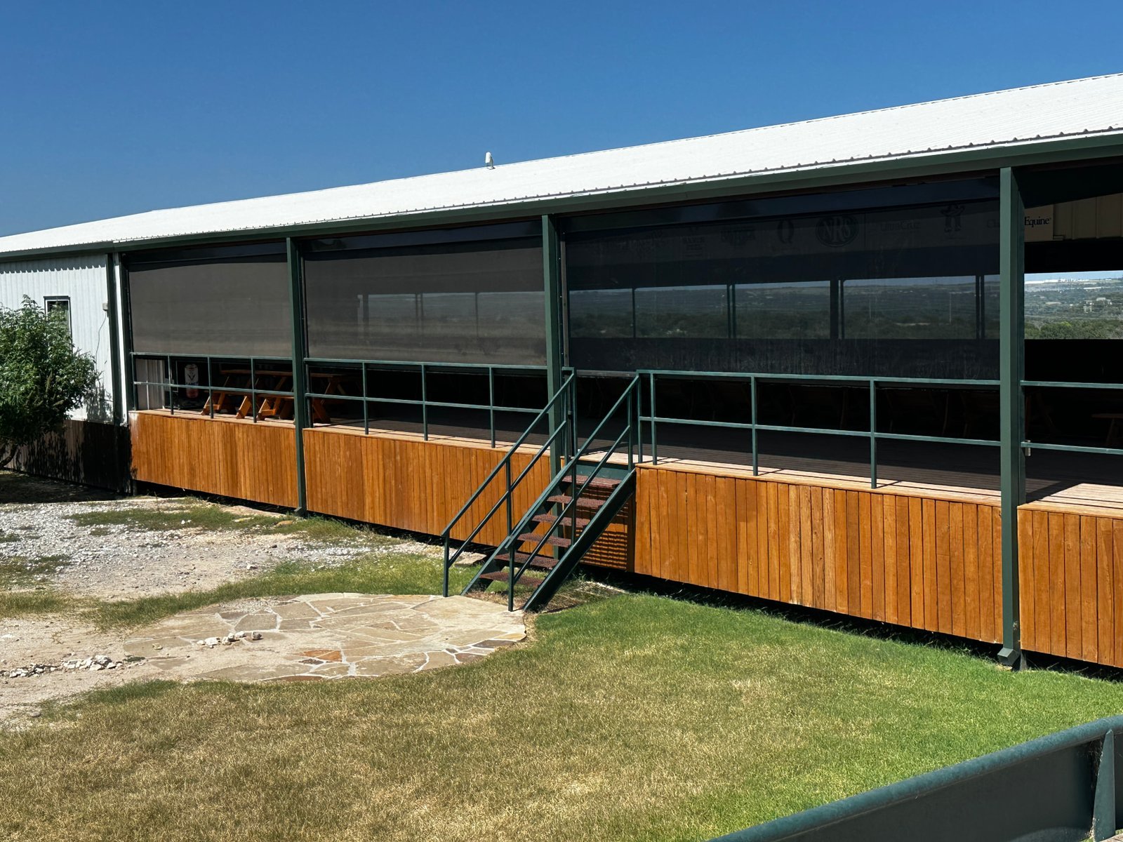 Real exterior photo of a ranch building with retractable screens and wooden deck skirting.