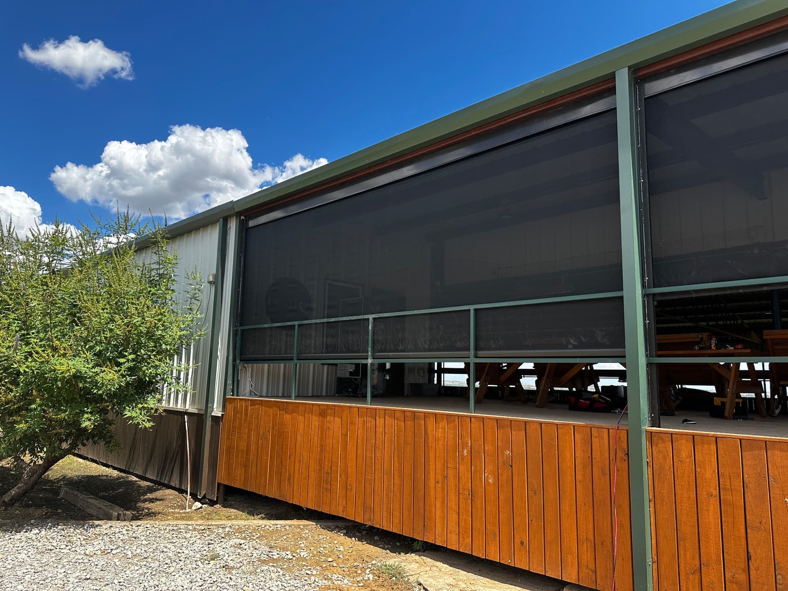 Real exterior photo of a ranch building with retractable screens and wooden deck skirting.