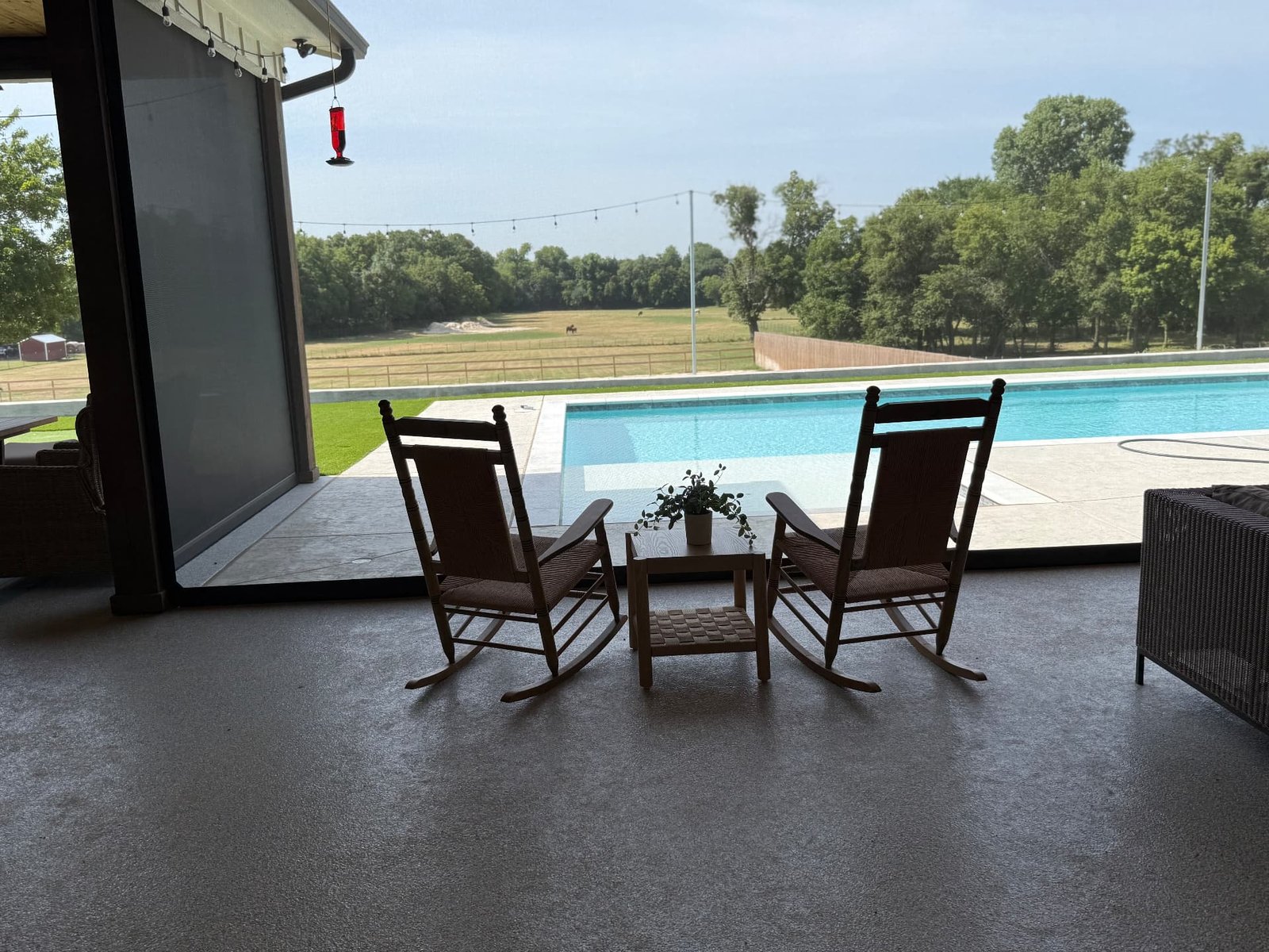 A covered patio with two wooden rocking chairs, a small table, and a view of the pool and open landscape beyond.
